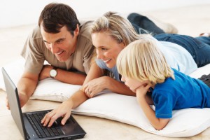 Happy couple with cute little boy using laptop while lying on floor